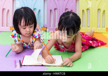 Cinese asiatici piccole sorelle la posa sul pavimento la colorazione a casa Foto Stock