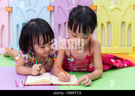 Cinese asiatici piccole sorelle la posa sul pavimento la colorazione a casa Foto Stock