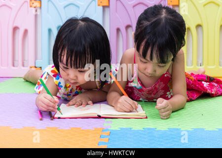 Cinese asiatici piccole sorelle la posa sul pavimento la colorazione a casa Foto Stock