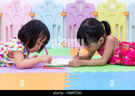 Cinese asiatici piccole sorelle la posa sul pavimento la colorazione a casa Foto Stock