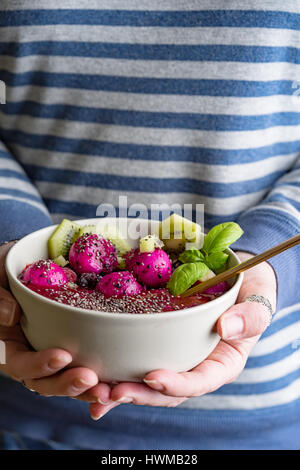 Donna di mani tenendo un colorato sano frullato casalinga ciotola con frutti rossi e basilico. Foto Stock