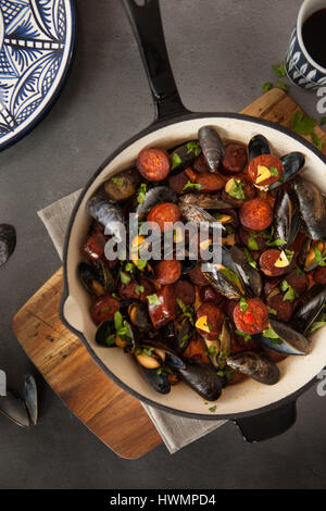 Surf and Turf: Una ciotola fatta in casa di cozze e chorizo servita in padella su un tavolo con una tavola e un piatto in stile spagnolo Foto Stock