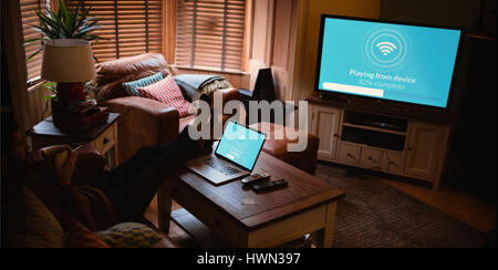 Immagine composita del testo con wi-fi simbolo contro l uomo con il computer portatile sul tavolo di guardare la televisione Foto Stock