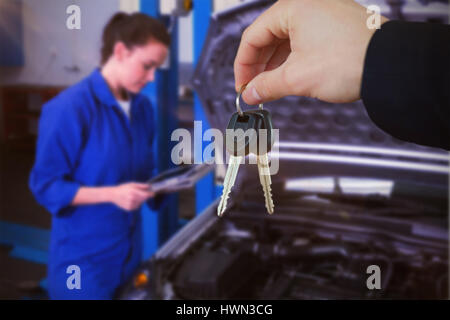 Donna sorridente mentre riceve le chiavi dell'auto contro meccanico utilizzando tablet per fissare l'auto Foto Stock