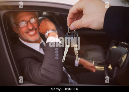 Donna sorridente mentre riceve le chiavi dell'auto contro il ritratto di imprenditore bello Foto Stock