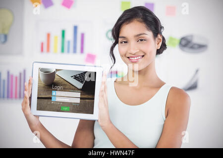 Felice imprenditrice che mostra digitale compressa in ufficio creativo contro close-up della pagina di login Foto Stock