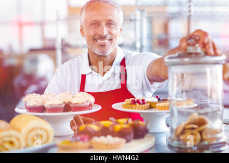 Immagine grafica di flare contro il ritratto di felice barista dietro le piastre di torte Foto Stock