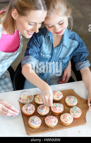 Elevato angolo di vista la figlia e la madre come decorare le tortine Foto Stock