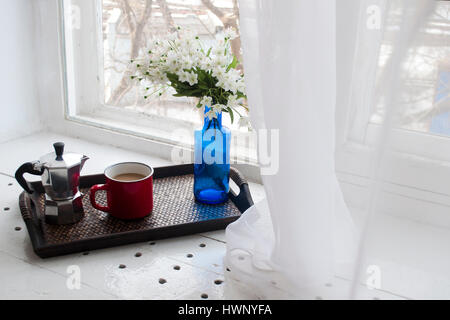 Tazza di caffè con un vaso blu su un vassoio di legno vicino alla finestra Foto Stock