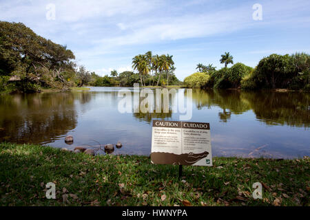 Avvertimento cartello di coccodrillo accanto allo stagno, Fairchild Tropical Botanic Garden in Coral Gables, Florida Foto Stock