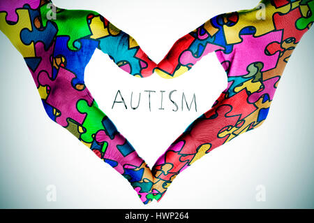 Donna mani formando un cuore modellato con molti pezzi di un puzzle di diversi colori, simbolo dell'autismo la consapevolezza e il testo autismo, con una leggera Foto Stock