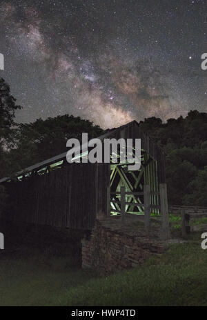 Il legno vecchio ponte coperto a Locust Creek vicino a Hillsboro, West Virginia si trova al di sotto della via lattea su una oscura notte chiara, il bagliore di luce all'interno. Foto Stock