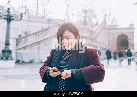 Giovane bella curva caucasica donna outdoor nella città di back light utilizzando smart phone e smartwatch- tecnologia, social network, comunicazione conce Foto Stock