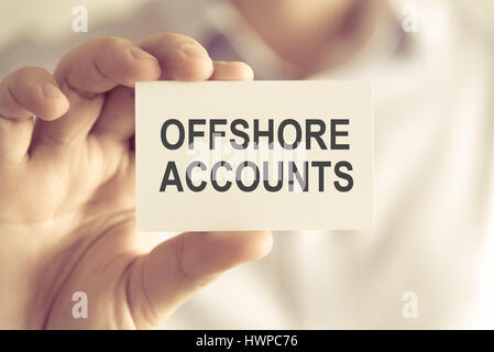 Primo piano sul proprietario in possesso di una carta con testo CONTI OFFSHORE , business Concetto di immagine con soft focus background e tono vintage Foto Stock
