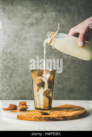 Mano d'uomo versando il latte per il caffè di cubetti di ghiaccio nel bicchiere Foto Stock