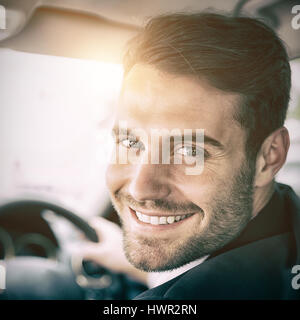 Uomo seduto in un auto e tenendo premuto uno smartphone sorridente in telecamera Foto Stock