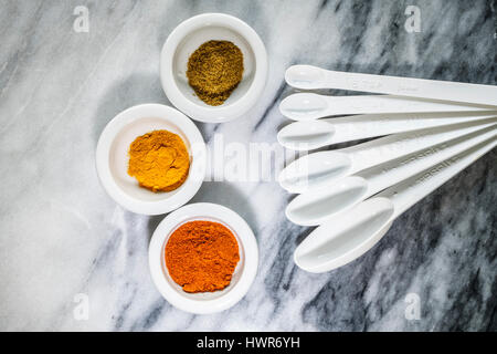 Posa piatto immagine di tre piatti bianchi di spezie colorate con set di plastica misurini su sfondo marmo. La curcuma, il cumino e la paprika. Foto Stock