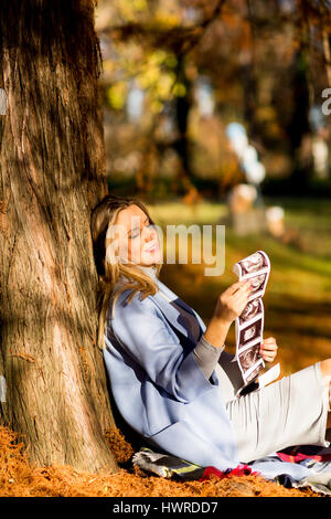 Giovane donna incinta seduta in autunno park e guardando atultrasounds foto di baby Foto Stock