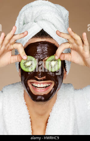 Laughing Man ricevere trattamenti spa. Foto del giovane con pezzi di kiwi nei suoi occhi e cioccolato maschera facciale. Beauty & Skin care concept Foto Stock