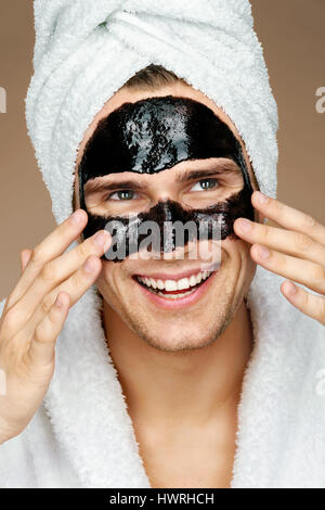 Uomo felice con maschera nera sul volto. Foto di ben curato uomo ricevere trattamenti spa. Beauty & Skin care concept Foto Stock