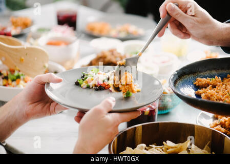Ritagliate la mano dell'uomo che serve il riso a femmina amico al tavolo da pranzo in party Foto Stock