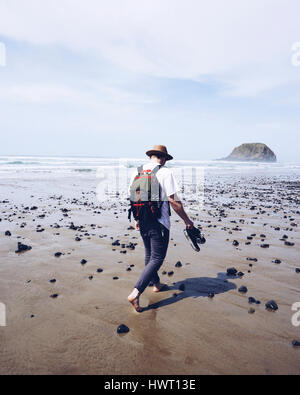 Vista posteriore di un escursionista a piedi su bagnato spiaggia sabbiosa contro sky durante la giornata di sole Foto Stock