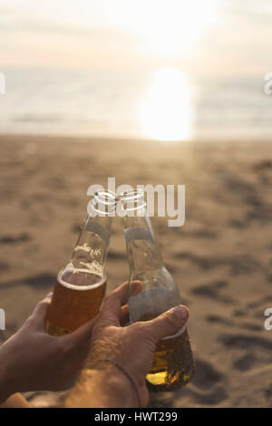 Mani tagliate di amici della birra di tostatura in spiaggia durante il tramonto Foto Stock
