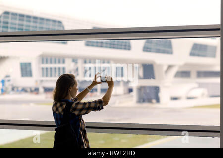 Donna fotografare attraverso la finestra mentre in piedi in aeroporto area di partenza Foto Stock