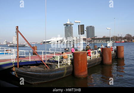 Piattaforma per il pedone e bicicletta traversata in traghetto a IJ River in Amsterdam, un'DAM torre occhio e Museo dei film in background Foto Stock