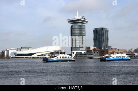 Pedone e bicicletta Ferries crossing presso il fiume IJ dietro la stazione centrale di Amsterdam, Paesi Bassi. Occhio film museum & UN'DAM torre in background Foto Stock