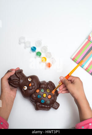 Mani corte di ragazza che decora il coniglietto di cioccolato pasquale a casa Foto Stock