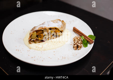 Un pezzo di strudel apetite con Orange, dado, cannella pod su una piastra bianca Foto Stock