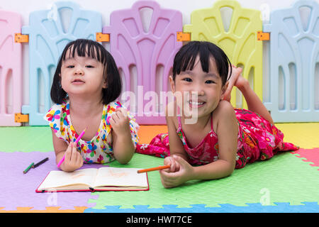 Felice cinese asiatici piccole sorelle la posa sul pavimento la colorazione a casa Foto Stock