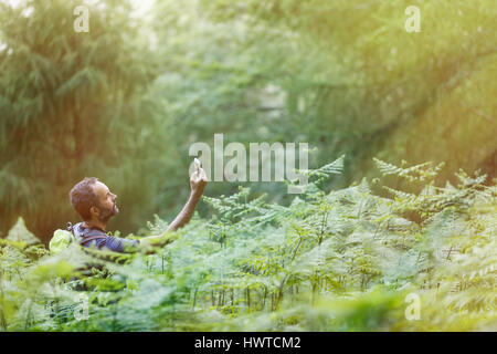 Gli escursionisti alla ricerca di un telefono cellulare segnale, persa nel lussureggiante foresta illuminata dalla brillante luce del sole dorato. Uno stile di vita attivo, la vita moderna, depen tecnologico Foto Stock