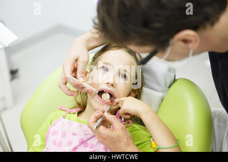 Poco ragazza seduta sulla poltrona odontoiatrica in pazienti pediatrici dentisti office, in corso di esame da parte del suo medico dentista. La prevenzione precoce, igiene orale e dei denti di latte co di cura Foto Stock