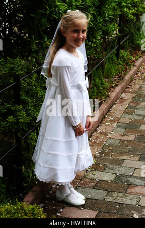 Prima Santa Comunione bambina in piedi in giardino che indossa il suo abito bianco e il velo Foto Stock