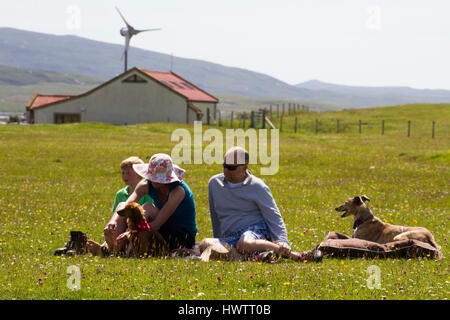 Famiglia rilassante godendo la visione di sport competitivo come parte del Festival Berneray taing posto sulla fioritura machir , precedentemente in estate habitat di nidificazione di poco sterne . Sala comunitaria del Borve dietro con fonti di energia rinnovabili turbina eolica . Foto Stock