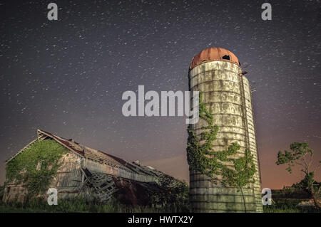 Tra i invadendo l'ambiente, un vecchio silo e fienile stand a Mason County, West Virginia con una lunga esposizione che mostra il movimento delle stelle. Foto Stock