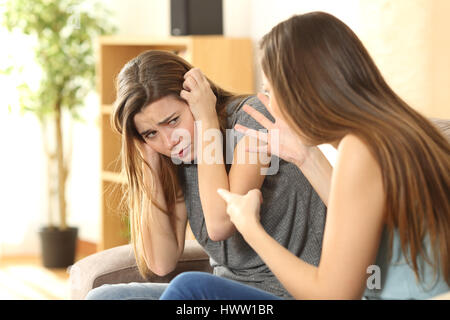 Ragazza rimproveri per la sua paura sorella o amico seduto su un divano nel soggiorno in un interno di una casa Foto Stock