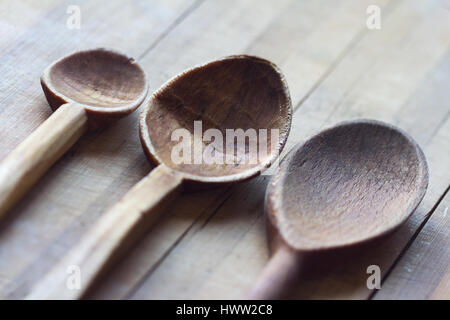 Vista laterale di tre realizzato a mano in legno cucchiai da cucina di dimensioni e forme diverse su un legno tagliere il fuoco selettivo copyspace Foto Stock