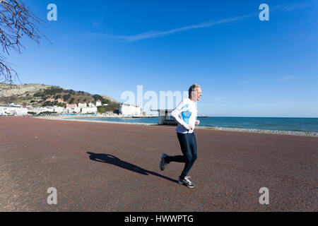 Uomo correre tutto solo lungo la promenade presso la famosa cittadina balneare di Llandudno, la mattina presto prima che la folla arrivare Foto Stock