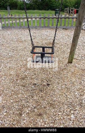 Park swing per un giovane bambino dove la corteccia scheggiata è lontano da indossare sotto. Recinzione, inferriata, erba e alberi in background. Foto Stock