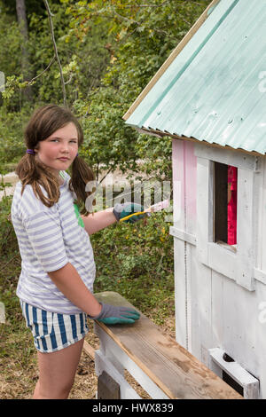 La ragazza la verniciatura esterna di una piccola playhouse fuori in giardino in estate Foto Stock