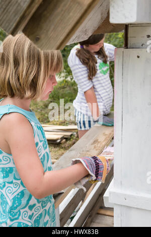 I bambini la verniciatura esterna di una piccola playhouse assieme al di fuori in giardino in estate Foto Stock