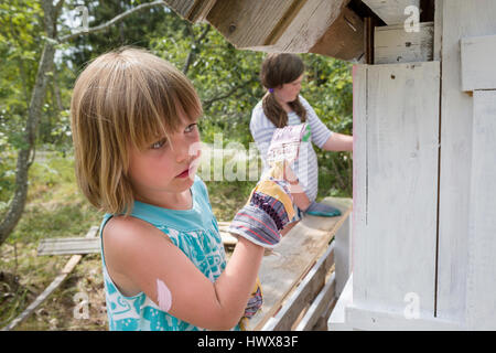 I bambini la verniciatura esterna di una piccola playhouse assieme al di fuori in giardino in estate Foto Stock