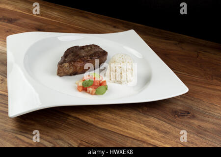 Fetta di grigliata di carne di vacca (picanha), riso e insalata su un piatto bianco e legno naturale tabella Foto Stock