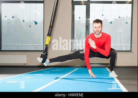 Ricci bianco barbuto uomo sportivo esercitando con cinghie di fitness in palestra Foto Stock