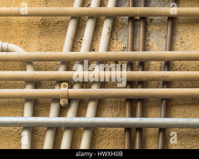 Modello geometrico di un gruppo di incrocio e sovrapposizione dei tubi di acqua su un intonacata parete ocra Foto Stock