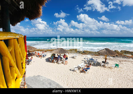 Giornata soleggiata con cielo nuvoloso sulla sabbia spiaggia con ombrelloni di paglia e turisti su Cozumel Foto Stock