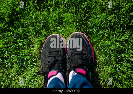 Selfie dei piedini femmina sul nero sneakers in piedi su erba verde Foto Stock